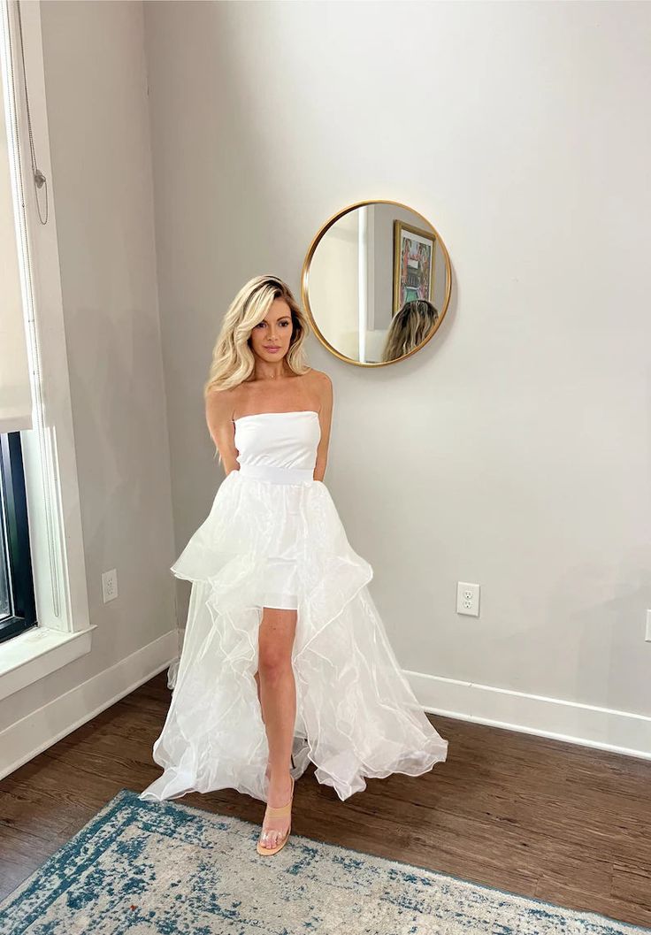 a woman standing in front of a mirror wearing a white dress with ruffles