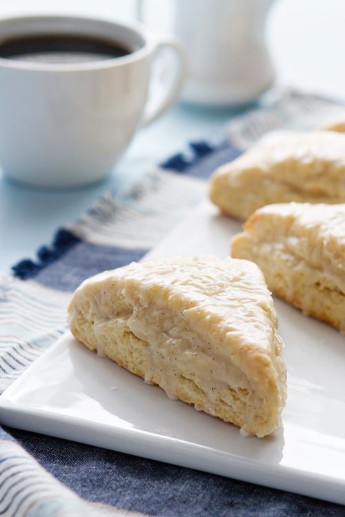 two scones on a white plate with a cup of coffee in the back ground