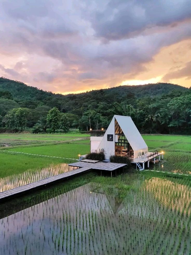 a small house sitting on top of a lush green field next to a lake at sunset