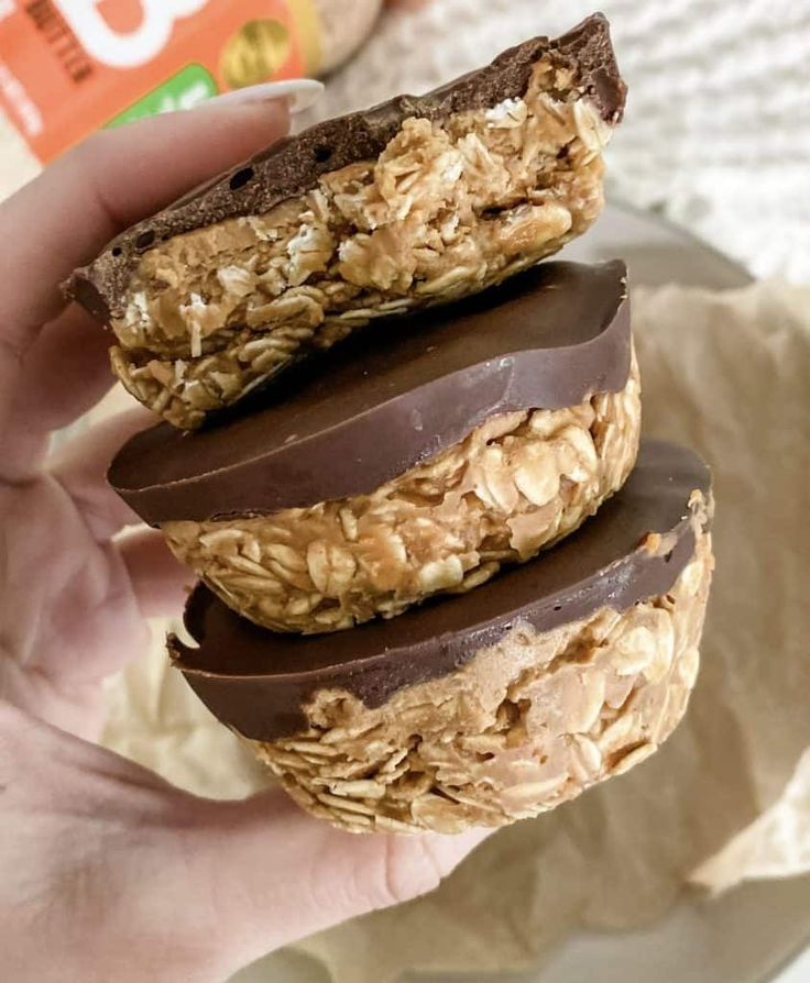 a person holding three chocolate covered cookies in their left hand and an oatmeal on the other