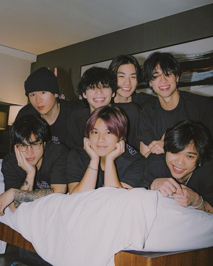 a group of young men posing for a photo on a bed with their arms around each other