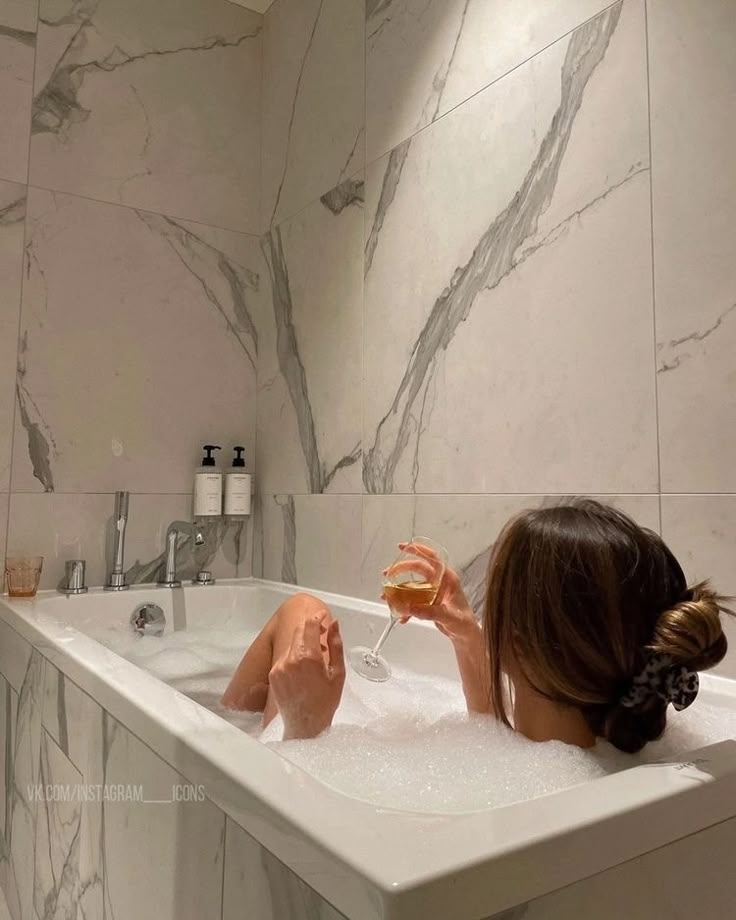 a woman sitting in a bathtub holding a glass of wine