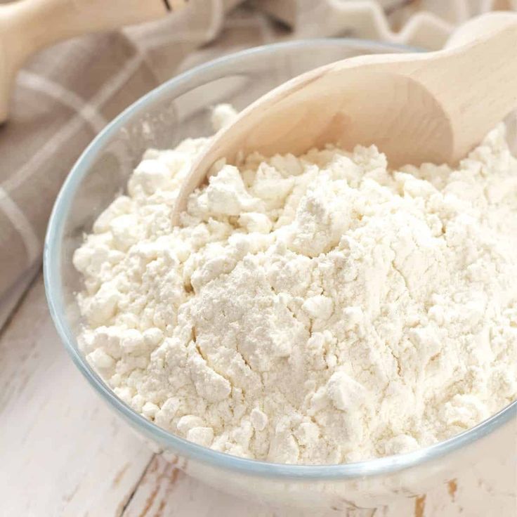 a wooden spoon in a bowl filled with white flour on top of a tablecloth