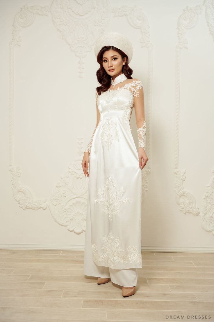 Step into elegance and grace with our Daxia White Vietnamese Ao Dai, a timeless and enchanting choice for your special day. With an illusion neckline and back, this gown creates an ethereal and captivating aura. Long sleeves add a touch of classic beauty, and the exquisite couture lace adorns the entire ensemble, adding a luxurious and intricate touch. To add a touch of grandeur to your bridal look, a sweeping train gracefully follows behind you, making your entrance truly unforgettable. Detail: White Vietnamese Ao Dai Collar: 1.6”/4cm Illusion neckline Illusion back Long sleeves Bra cups added Zipper closure White pants Couture lace Made to order Elegant Gown With Illusion Neckline For Debutante Ball, Elegant Formal Wedding Dress With Lace Back, Elegant White Mother Of The Bride Dress For Ceremony, Elegant Floor-length Wedding Dress For Ceremony, Floor-length Wedding Dress With Detachable Train For Ceremony, Elegant Floor-length Wedding Dress With Lace Back, White Sheer Bodice Evening Dress For Debutante Ball, Elegant White Gown With Lace Back, Wedding Evening Dress With Sheer Back And Fitted Bodice