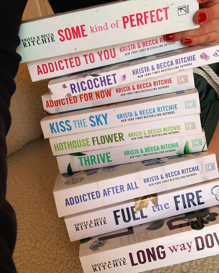 a stack of books sitting on top of a floor next to a woman's hand