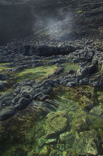 the sun shines through the clouds over some rocks and water