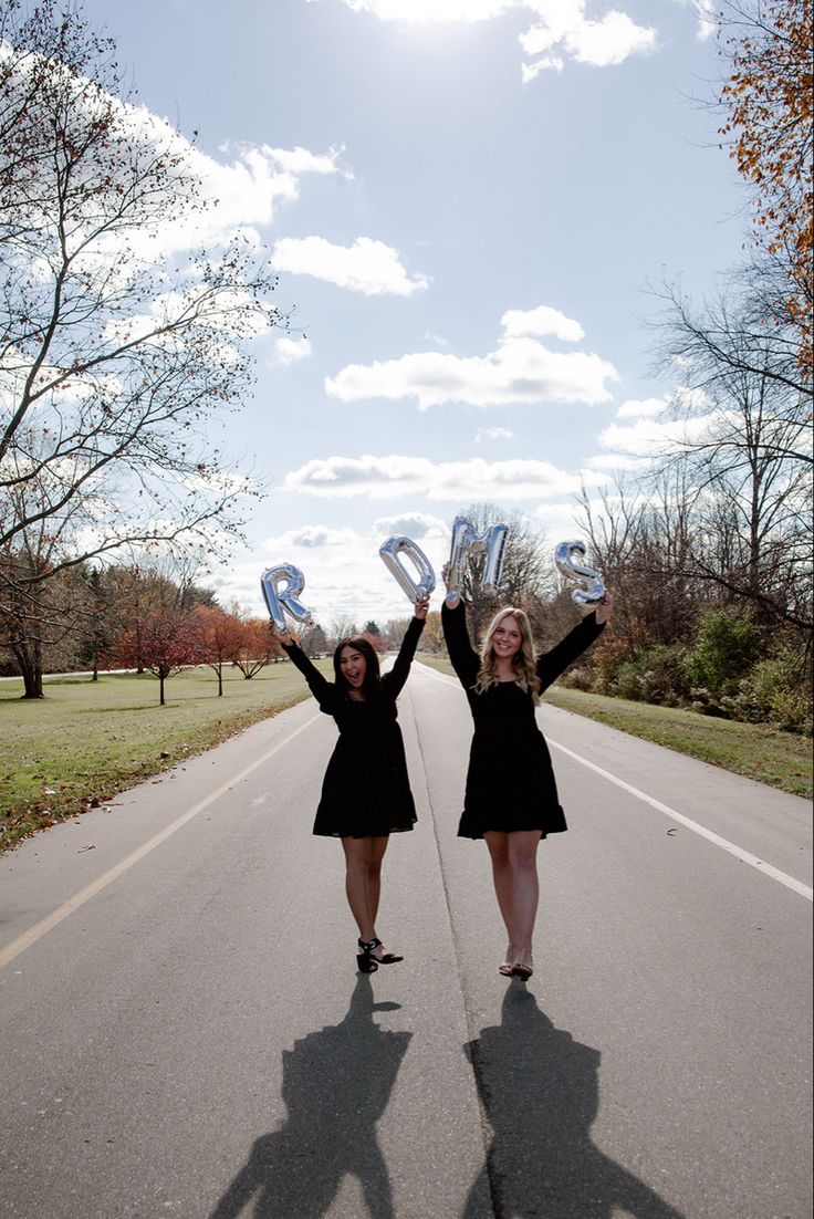 two women standing in the middle of a road holding up letters that spell out r