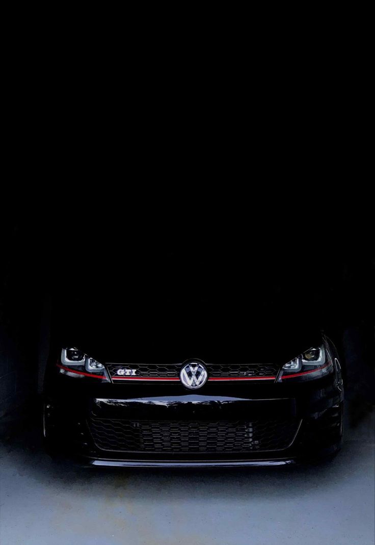 the front end of a black volkswagen car in a dark garage with its lights on