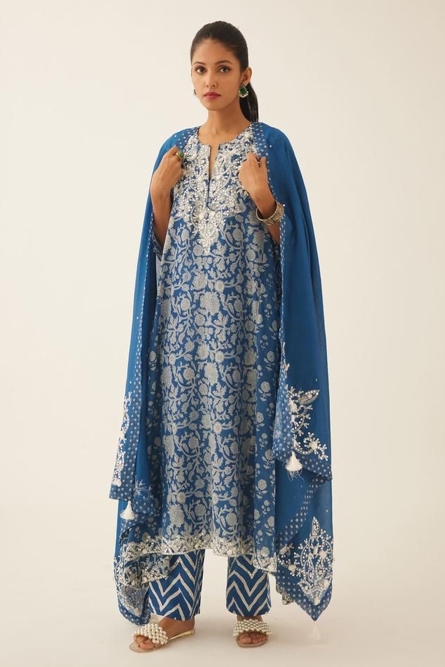 Blue asymmetric kalidar kurta with floral, mughal hand block print and sequin, tassel, bead work on neckline and sleeve hem. Paired with cotton slip, chevron hand block print straight pant and dupatta with printed border on the edges.
Components: 4
Pattern: Hand Block Printed, Embroidery
Type Of Work: Floral, chevron, sequin, bead, tassel
Neckline: Notched
Sleeve Type: Three quarter
Fabric: Kurta: Cotton Chanderi, Slip and Pant: Cotton, Dupatta: Silk Chanderi
Color: Blue
Other Details: 
Elastica Kurta Cotton, Printed Embroidery, Blue Kurta, Cotton Slip, Cotton Dupatta, Straight Pants, Set For Women, Aza Fashion, Sleeve Type