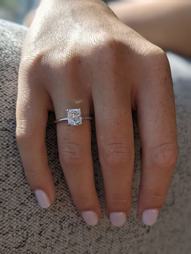 a woman's hand with a diamond ring on her left hand, sitting on a couch