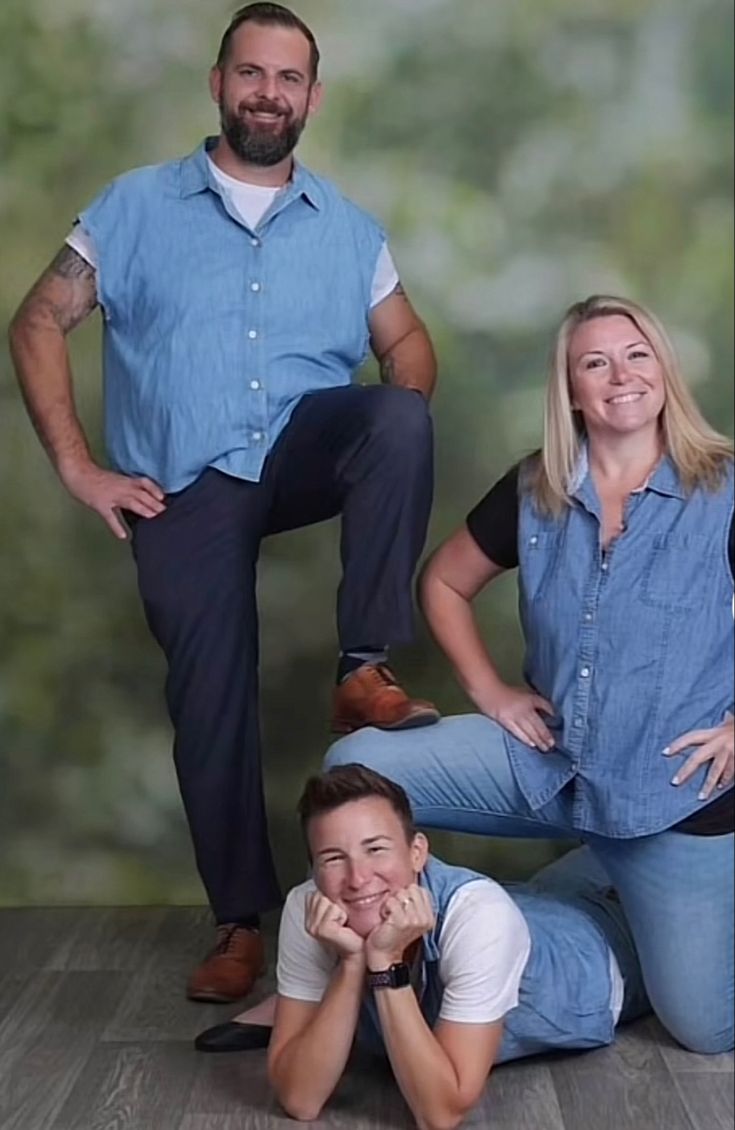 three people are posing for a photo in front of a green background, with one person leaning on the ground