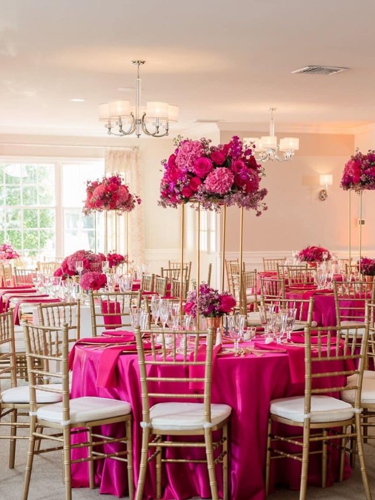 a room filled with lots of tables and chairs covered in pink table cloths next to tall flower centerpieces