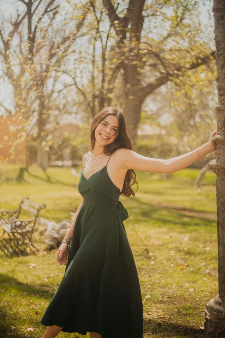 a woman in a green dress is posing for a photo near a tree with her arms outstretched