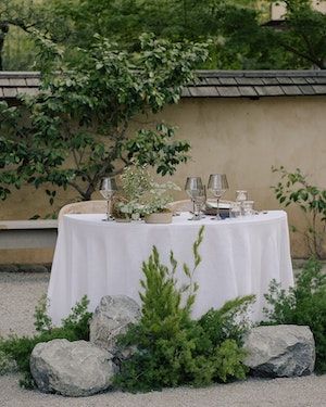 a table set up with wine glasses and plates on it in the middle of some rocks