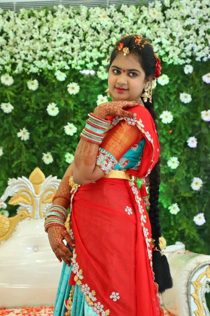 a woman in a red and blue sari posing for the camera with flowers behind her