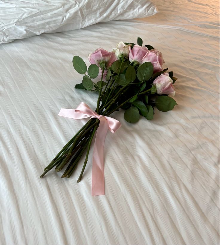 a bouquet of pink roses laying on top of a white bed with a pink ribbon