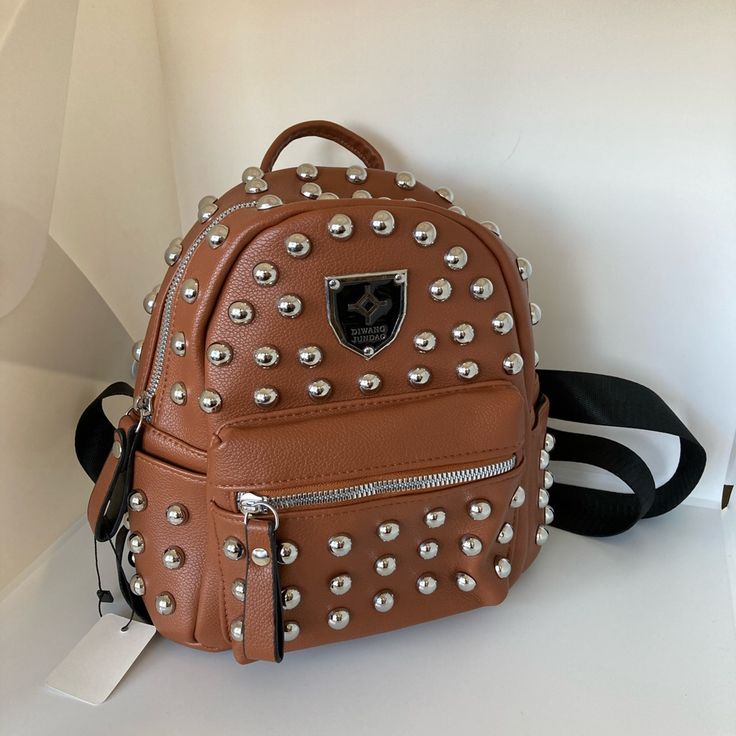 Golden Brown Backpack Purse With Studs Has A Loop To Hang Or Carry At Top Of Backpack Has 2 Slide In Pockets On Sides On The Outside Main Closure Double Zipper With Silver Stud And Hardware Has Zipper Pocket In Front For Cards And Smaller Items With Adjustable Straps For The Perfect Look And Fit Use This Bag For Your Everyday Bag Carry All Your Essentials And More And Look Great In This Backpack Perfect For People That Have A Lot Of Things To Carry And Always On The Go And It’s Light To Carry 9x Silver Backpack For Travel, Silver School Backpack, Silver Standard School Backpack, Silver Backpack For Everyday Use, Silver School Bag With Zipper Closure, Silver Standard Backpack For Daily Use, Trendy Silver Backpack For Travel, Trendy Silver Backpack For School, Silver Everyday Use Backpack