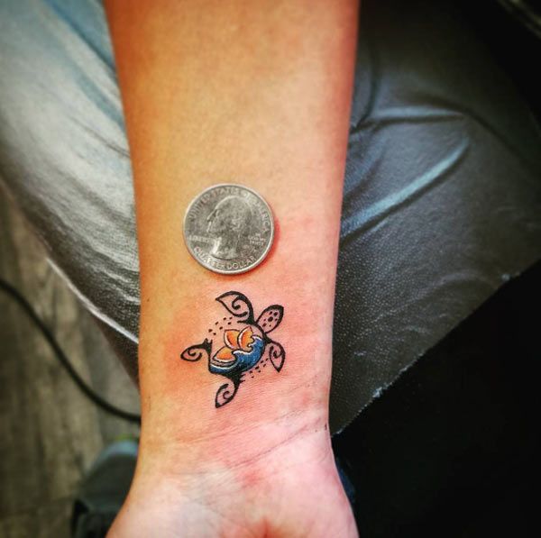 a small tattoo on the wrist of a person with a coin in front of it