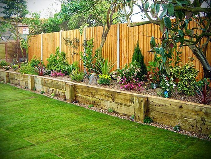 a wooden fence and some green grass in a back yard with plants on the side