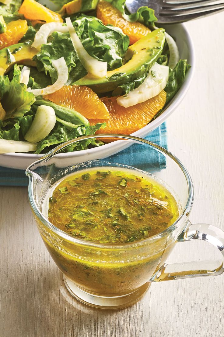 a salad with oranges and dressing in a bowl on a table next to a fork