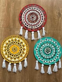 three colorful plates with tassels on top of a wooden floor next to each other