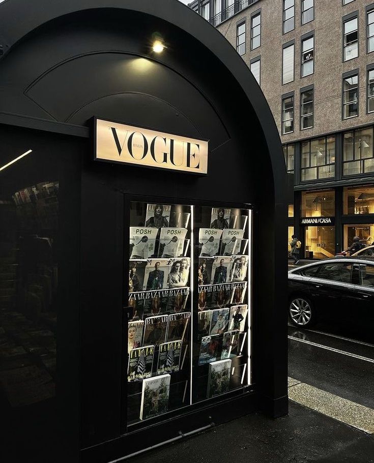 the front of a magazine store with cars parked in the street behind it on a rainy day