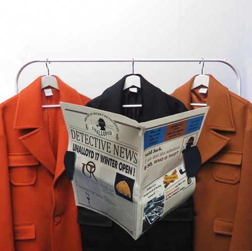 an orange coat is hanging on a rack and there is a newspaper in front of it