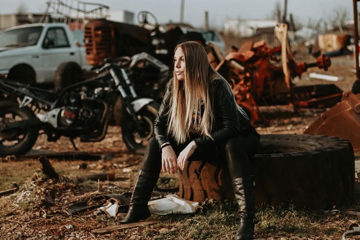 a woman sitting on top of a tree stump in front of a pile of junk