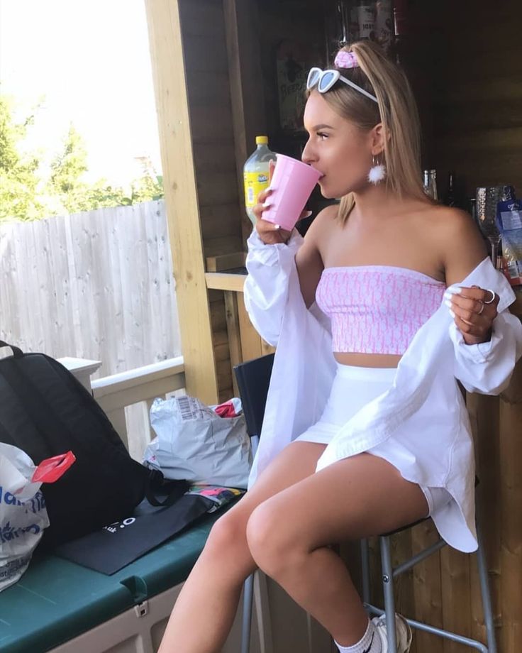 a woman sitting on top of a chair drinking from a pink cup and holding a drink in her hand