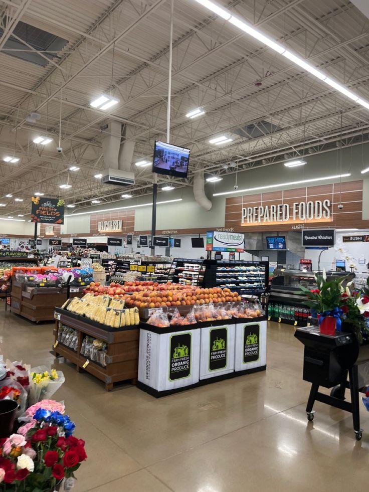 the produce section of a grocery store with flowers and fruits on display for sale in front of them