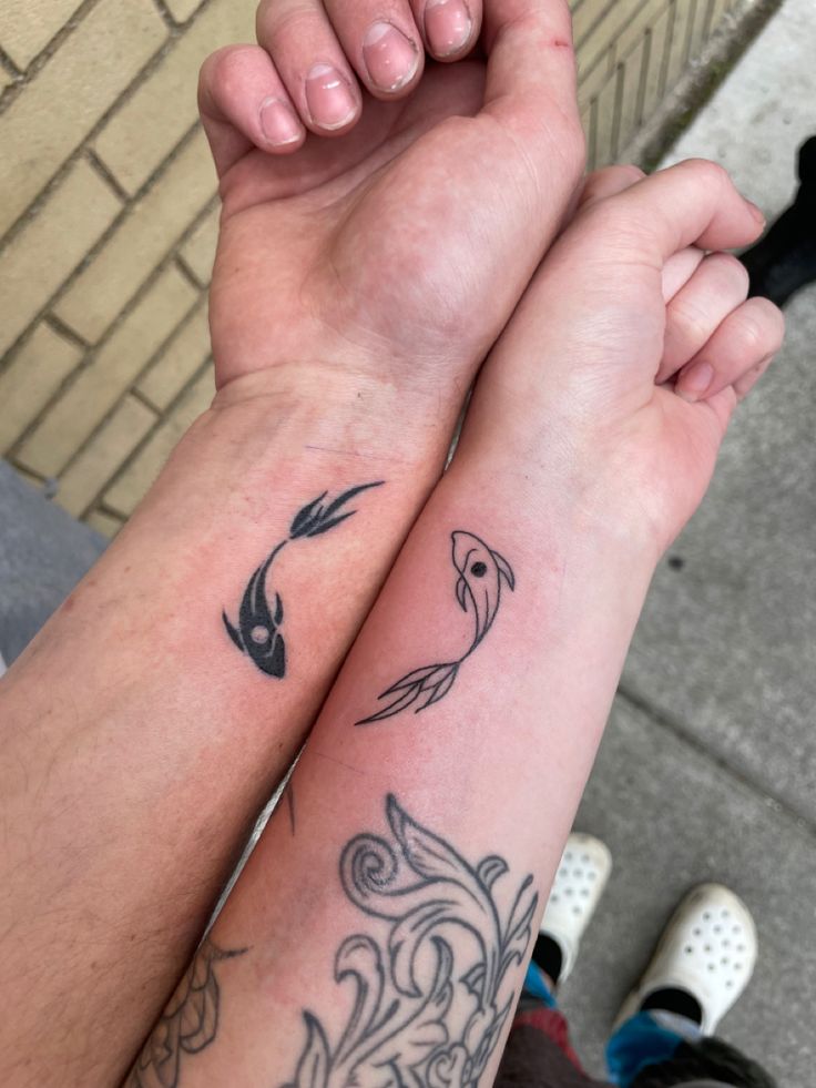 two people are holding hands with tattoos on their arms and armbands, one has a fish in the middle