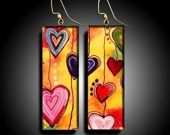 pair of earrings with hearts painted on them in yellow and pink colors, against a black background