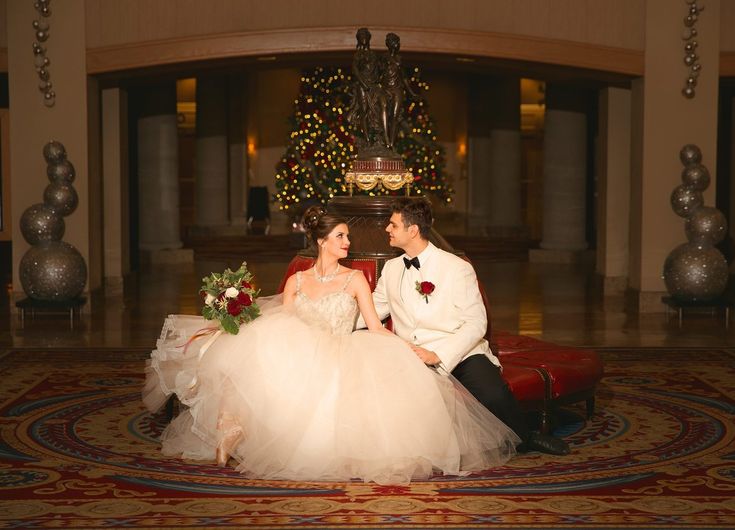 a bride and groom sitting on a red chair in front of a christmas tree