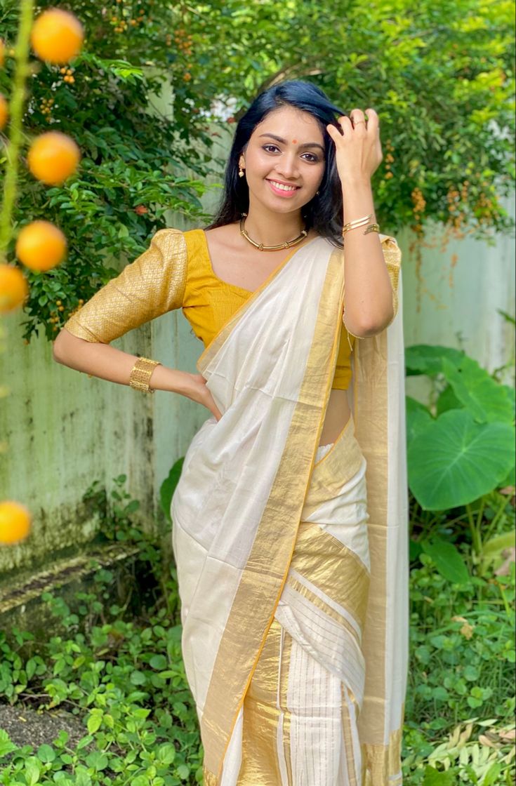 a woman in a yellow and white sari posing for the camera with her hand on her head