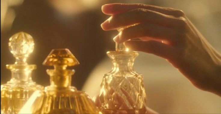 a person holding an object in their hand next to some perfume bottles on a table