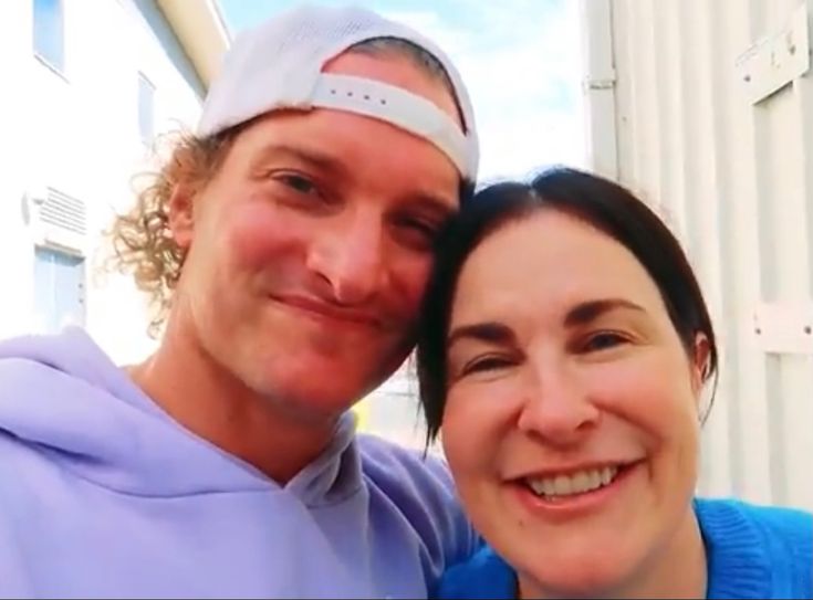 a man standing next to a woman in front of a white building and smiling at the camera