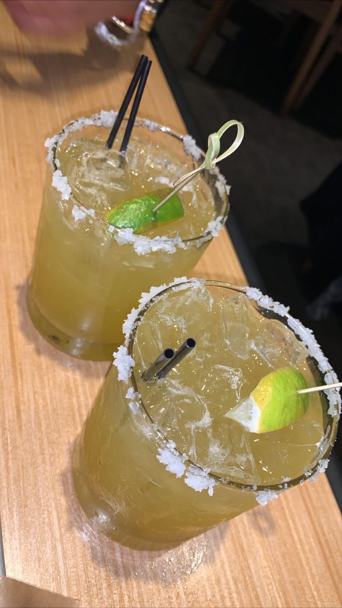 two margaritas sitting on top of a wooden table