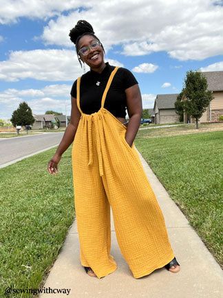 a woman standing on the sidewalk wearing a yellow jumpsuit and black t - shirt