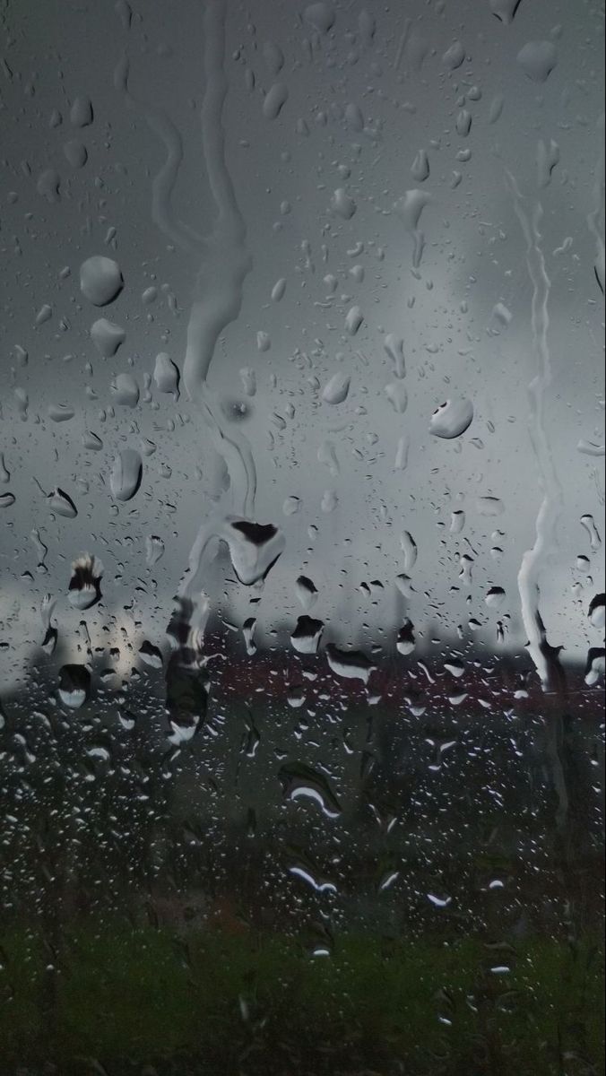 rain is falling down on the window and grass in the foreground, with an overcast sky behind it