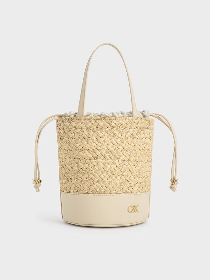 The quintessential bucket bag with a summer-friendly twist. This piece features a classic cylindrical shape, with a leather bottom offering a smooth contrast to the intricate woven finish and providing extra stability. It also includes a drawstring closure for quick and easy access to your belongings while keeping them safe and secure. The emblem adds a subtle touch of glamour in gold, further elevating this sophisticated design. Cheap Summer Cream Bucket Bag, Cheap Gold Bucket Bag, Luxury Straw Bucket Bag With Woven Leather, Luxury Woven Leather Straw Bucket Bag, Luxury Straw Bucket Bag With Bamboo Handle, Luxury Natural Straw Bucket Bag, Luxury Woven Straw Bucket Bag, Luxury Beige Basket Bucket Bag, Luxury Leather Summer Bucket Bag