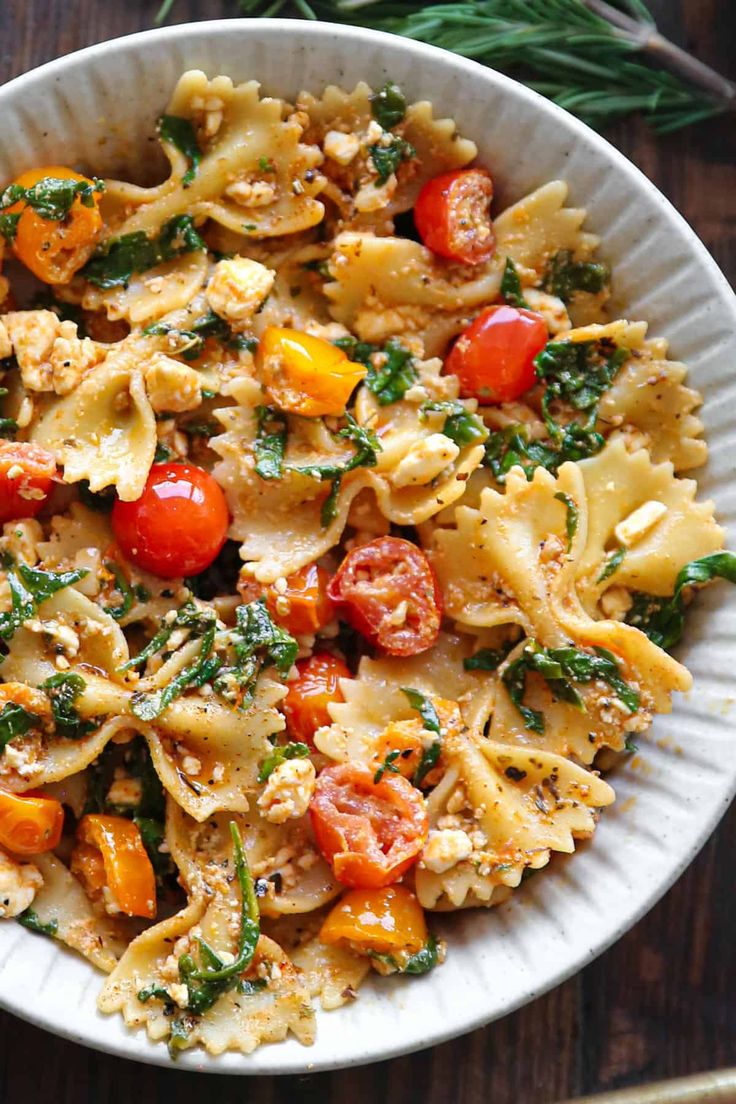 a white bowl filled with pasta, tomatoes and spinach on top of a wooden table