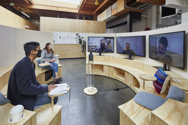 two people sitting in front of televisions on wooden desks with chairs around them