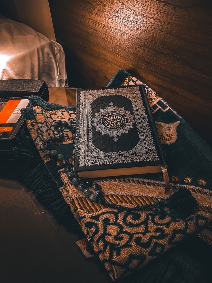 an open book sitting on top of a wooden table next to a lamp and blanket