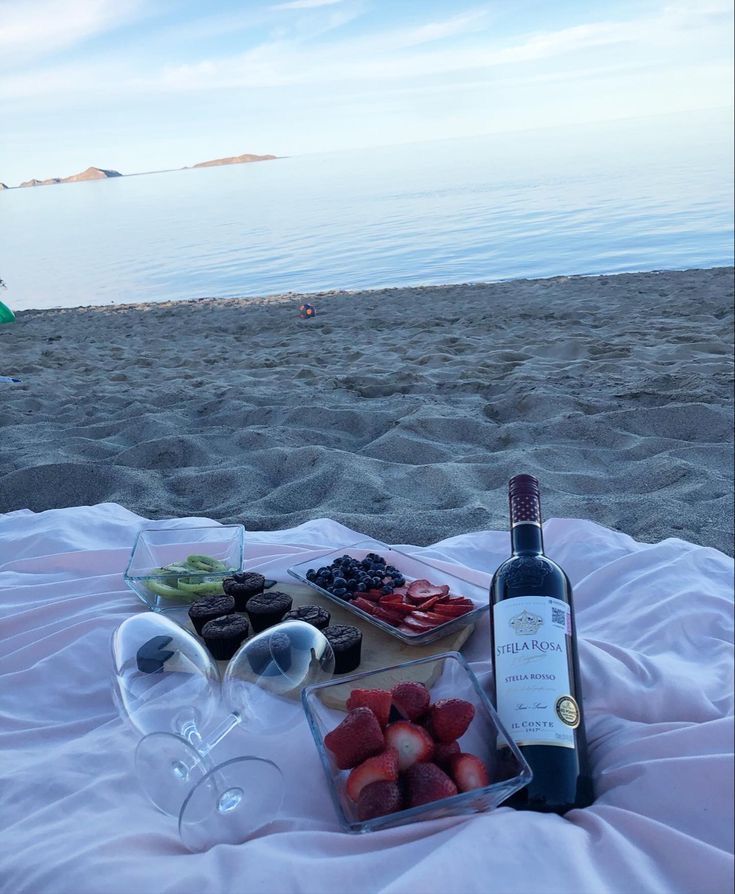 a bottle of wine sitting on top of a beach next to a plate of food