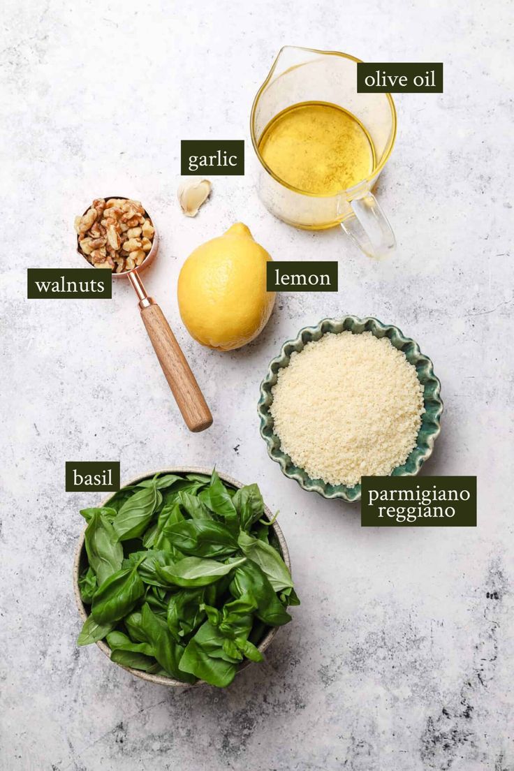 ingredients to make spinach salad laid out on a white counter top with lemons, walnuts, garlic, and parmesan