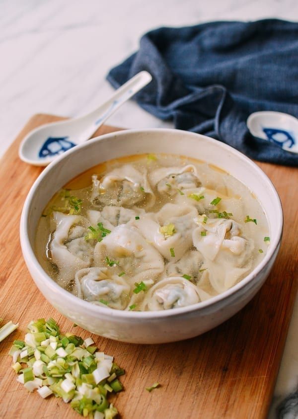 a wooden cutting board topped with a bowl of dumplings and celery next to a spoon