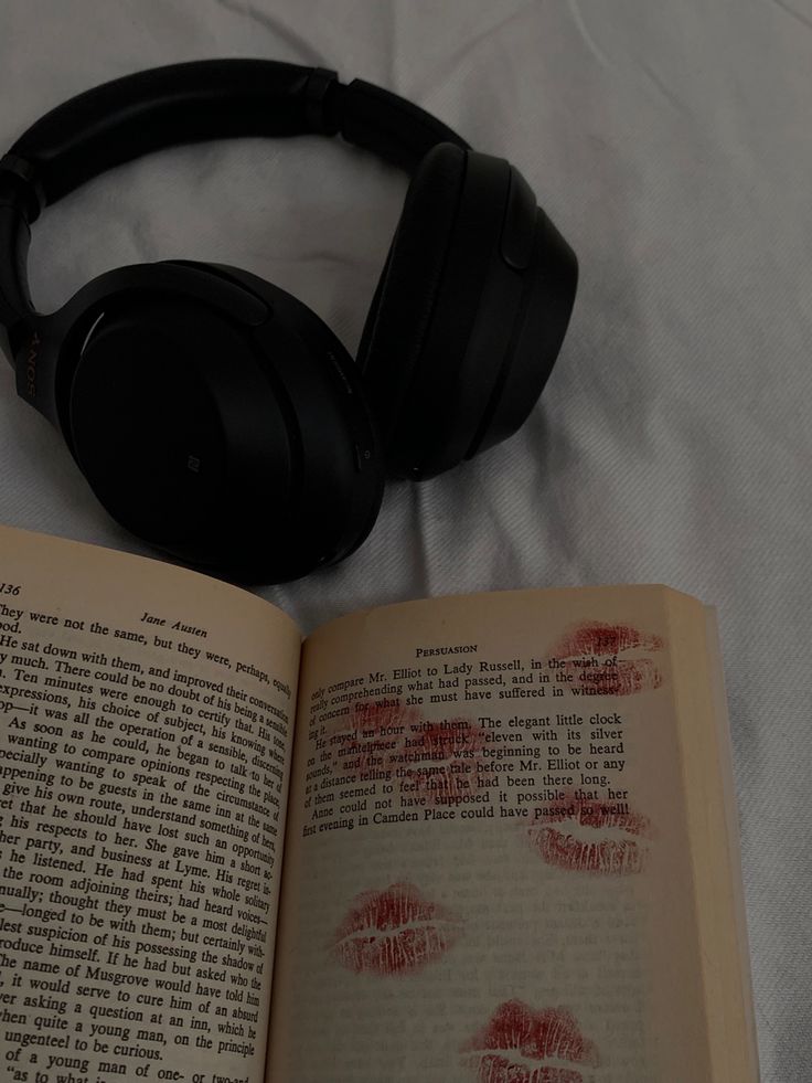 an open book with headphones on it next to a pair of red lipstick imprints