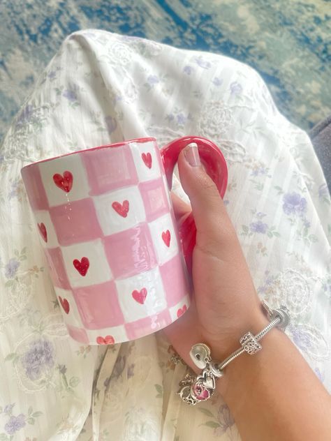 a woman's hand holding a pink and white coffee cup with hearts on it