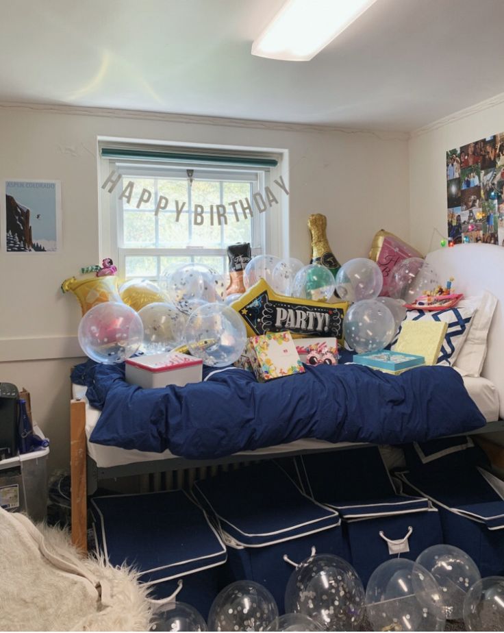 a birthday party with balloons, books and gifts on a bed in front of a window