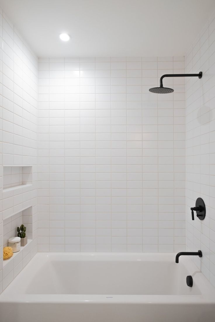 a white tiled bathroom with black fixtures and no shower head or faucet in it